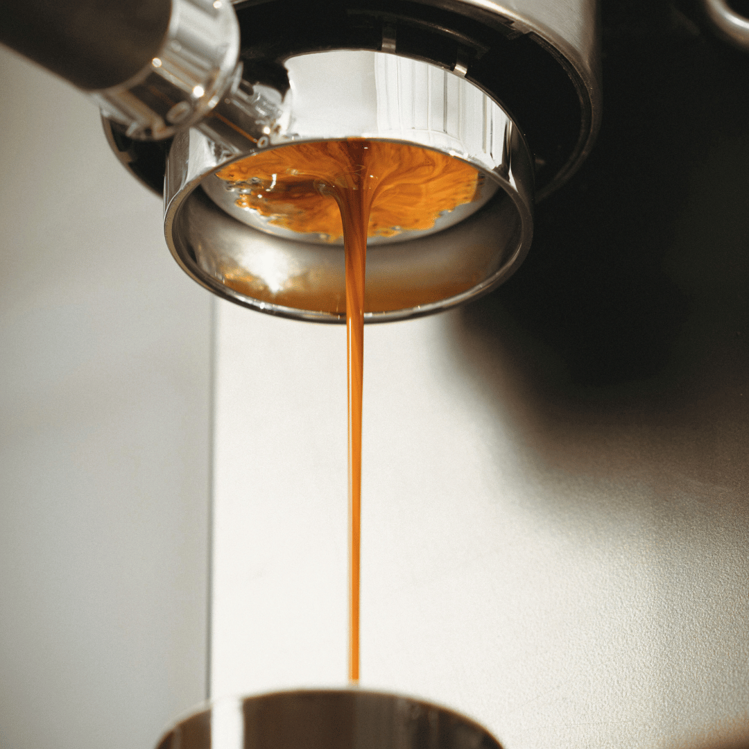 En dampende kop espresso ved siden af en espressomaskine og en pose friskristede kaffebønner – den perfekte kombination til kaffeelskere.