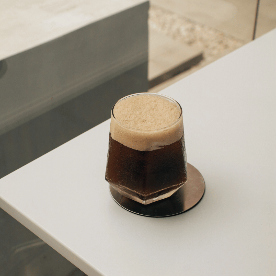 Cold Brew Tonic i et glas fyldt med isterninger, toppet med en citronskive – en forfriskende kaffedrik lavet med koldbrygget kaffe og tonicvand, perfekt til sommerens varme dage.