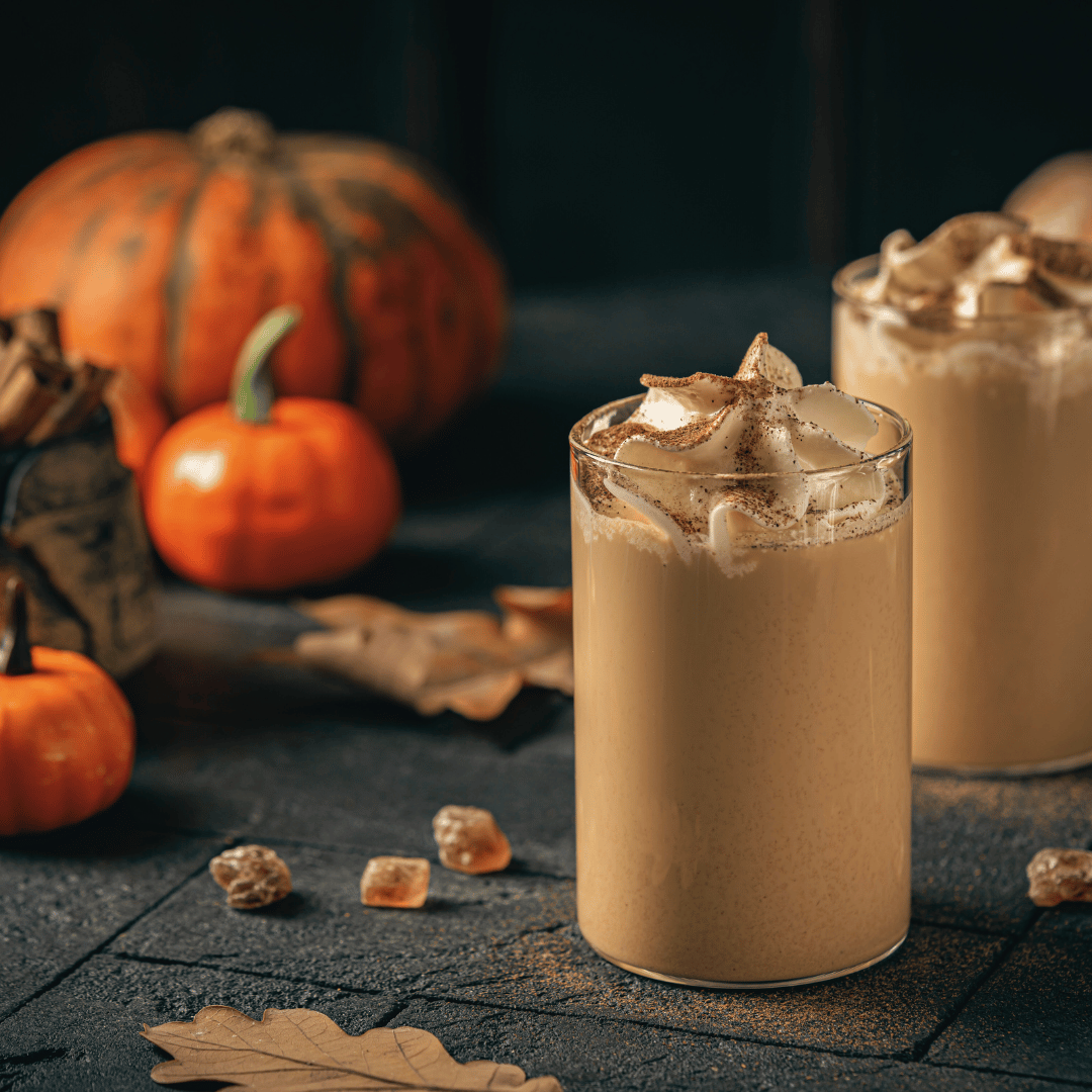 En kop hjemmelavet Pumpkin Spice Latte toppet med flødeskum og kanel, serveret med friskristet kaffe fra Rwanda – den perfekte efterårsdrik.