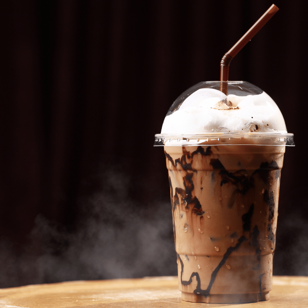 En lækker kaffemilkshake serveret i et glas, toppet med flødeskum og drysset med chokoladespåner, perfekt til kaffeelskere, der ønsker en kølende og cremet forfriskning.