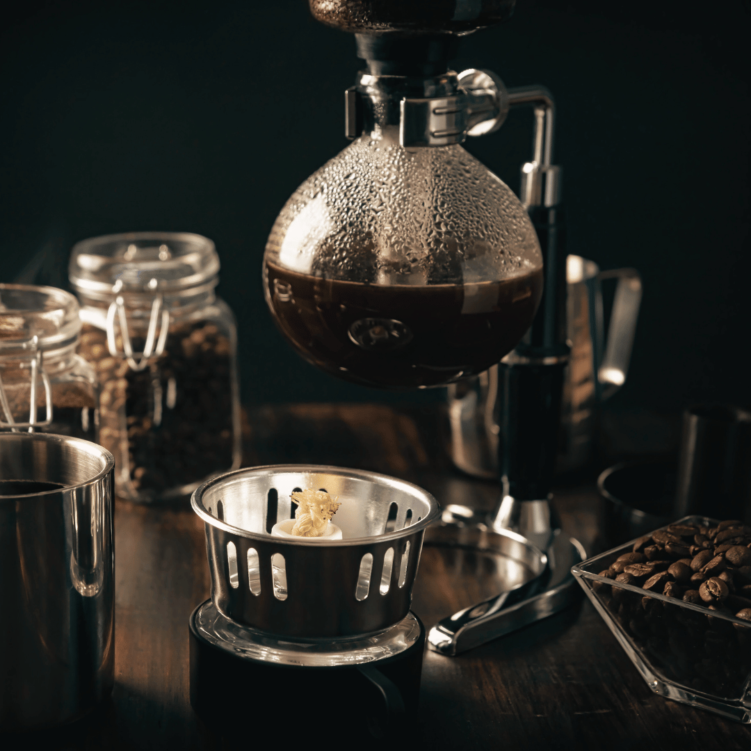  En siphon kaffebrygger i brug, der demonstrerer brygningens unikke vakuumproces. Perfekt til at skabe en ren og kompleks smagsoplevelse med friskristede kaffebønner, som vores mellemristede kaffe fra Rwanda eller lysristede kaffe fra Tanzania.