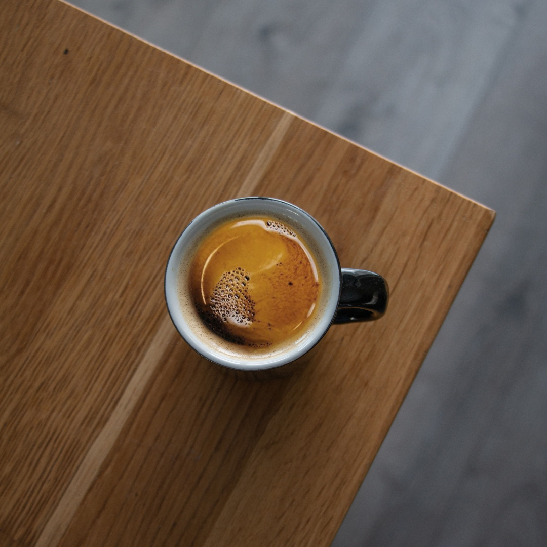 En kop Americano kaffe lavet med mørkristede bønner fra Brasilien, serveret i en hvid kop på et træbord.